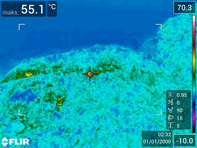 Lämpökuva, jossa näkyy maisema ja lämpötilalukemat; kuumin kohta on 55,1 °C keskellä, sitä ympäröivät viileämmät siniset alueet. Tietojen päällekkäisyyksissä näkyvät asetukset ja mittaukset sekä aikaleima ja FLIR-brändi.