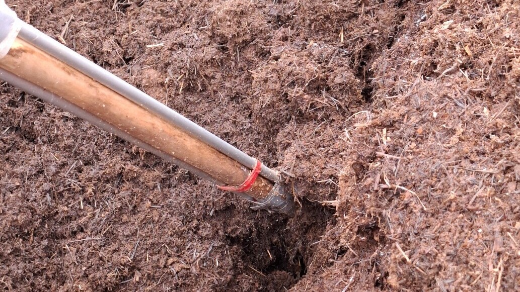 Lähikuva lapiosta, joka kaivaa löysää, ruskeaa maata tai kompostia niin, että lapion terä on osittain upotettu maahan.