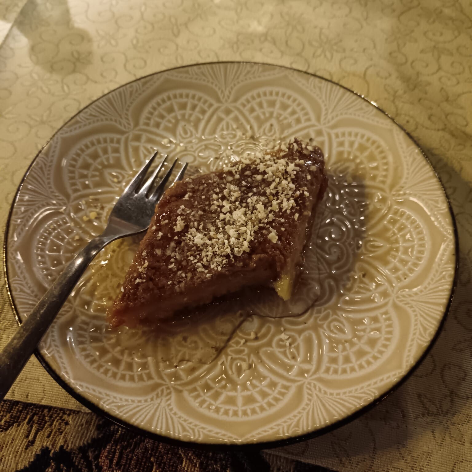 Jälkiruokaviipale, jonka päällä on tomusokeria, istuu koristeellisella, kuviollisella lautasella, jonka vieressä on haarukka, koristeellisen pöytäliinan päällä.