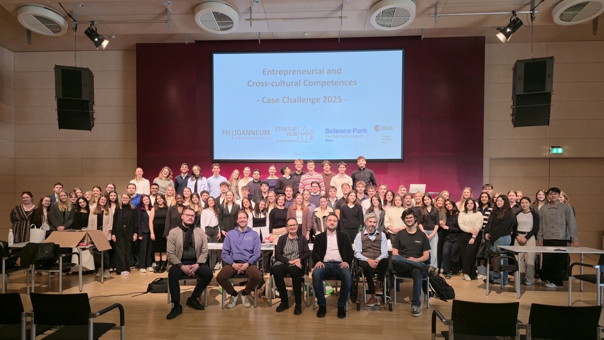 Suuri joukko ihmisiä poseeraa yhdessä luentosalissa näytön edessä, jossa näkyy Yrittäjyys- ja kulttuurienvälinen osaaminen - Case Challenge 2025. Osa istuu ja suurin osa seisoo hymyillen kameralle.