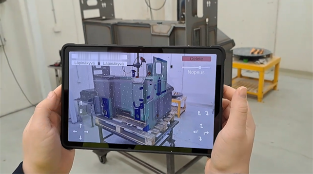 Henkilö pitää kädessään tablettia, joka näyttää teollisten komponenttien lisätyn todellisuuden päällekkäisyyttä, ja kohdistaa virtuaaliset elementit fyysisiin koneisiin työpajan ympäristössä.