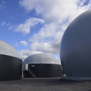 Suuria, pyöreitä, kupolimaisia teollisuusrakennuksia, joissa on sileät harmaat ja valkoiset pinnat osittain pilvisen sinisen taivaan alla; yhteen kupoliin johtaa pieni portaikko, ja oikealla näkyy osa pysäköidystä autosta.