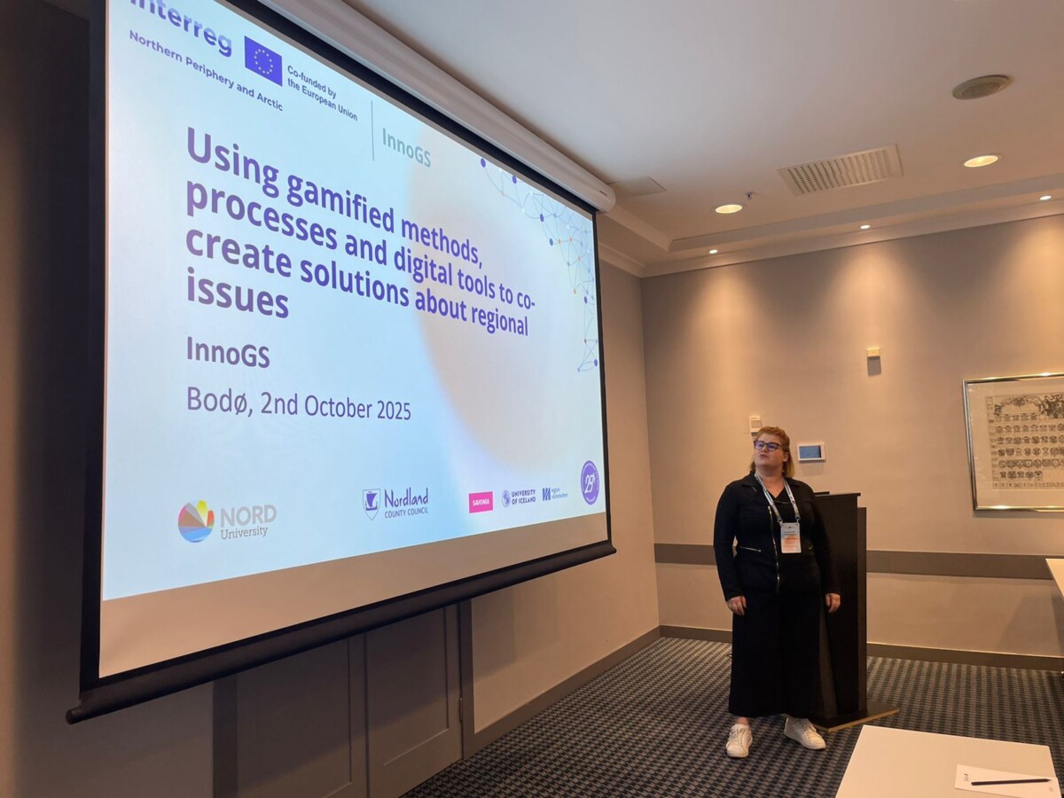Nainen seisoo valkokankaan vieressä esityksessä "Pelillisten menetelmien, prosessien ja digitaalisten työkalujen käyttäminen alueellisten kysymysten ratkaisujen yhteiskehittämiseen", joka pidettiin Bodøssä 2. lokakuuta 2025.