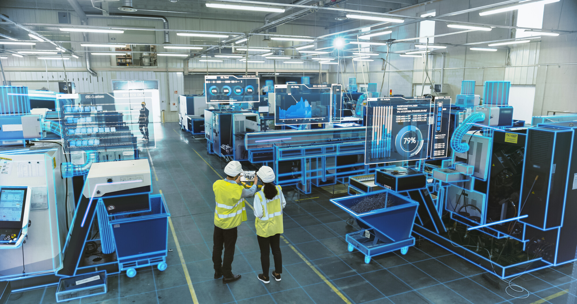 Kaksi turvaliiviin ja kypärään pukeutunutta ihmistä seisoo modernissa tehtaassa katselemassa digitaalisia näyttöjä ja kehittyneitä koneita, joissa sininen hologrammi korostaa älykkään teknologian integrointia.