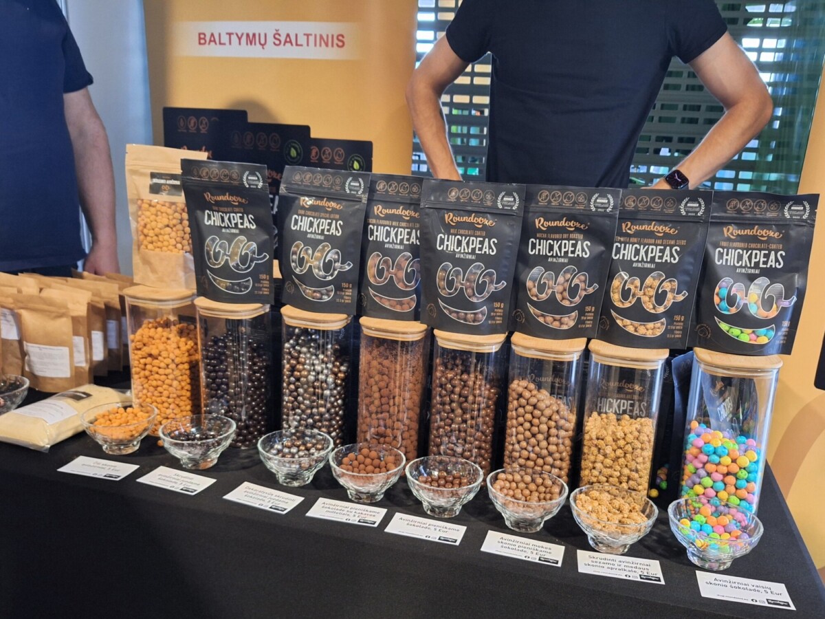 Eri makuja sisältäviä paahdettuja kikherneitä lasipurkeissa ja -kulhoissa, ja jokaisen purkin takana on etiketöity pakkaus. Kaksi ihmistä seisoo pöydän takana myyntikojussa.