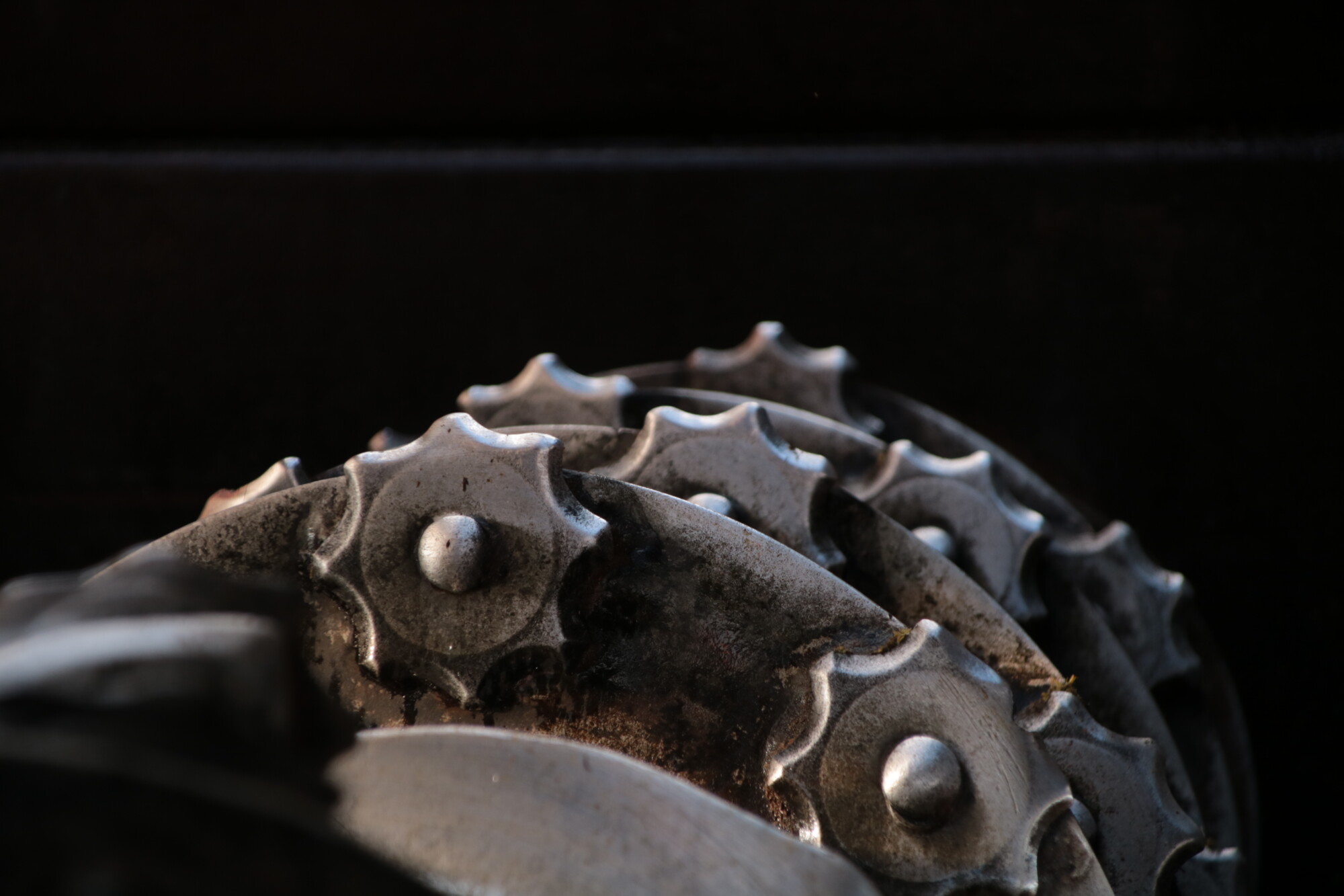 Lähikuva useista metallisista hammaspyöristä, joissa on tähdenmuotoiset hampaat ja jotka ovat osittain päällekkäin tummaa taustaa vasten. Hammaspyörissä on kulumisen ja ruosteen merkkejä, mikä luo teollisen ja mekaanisen vaikutelman.