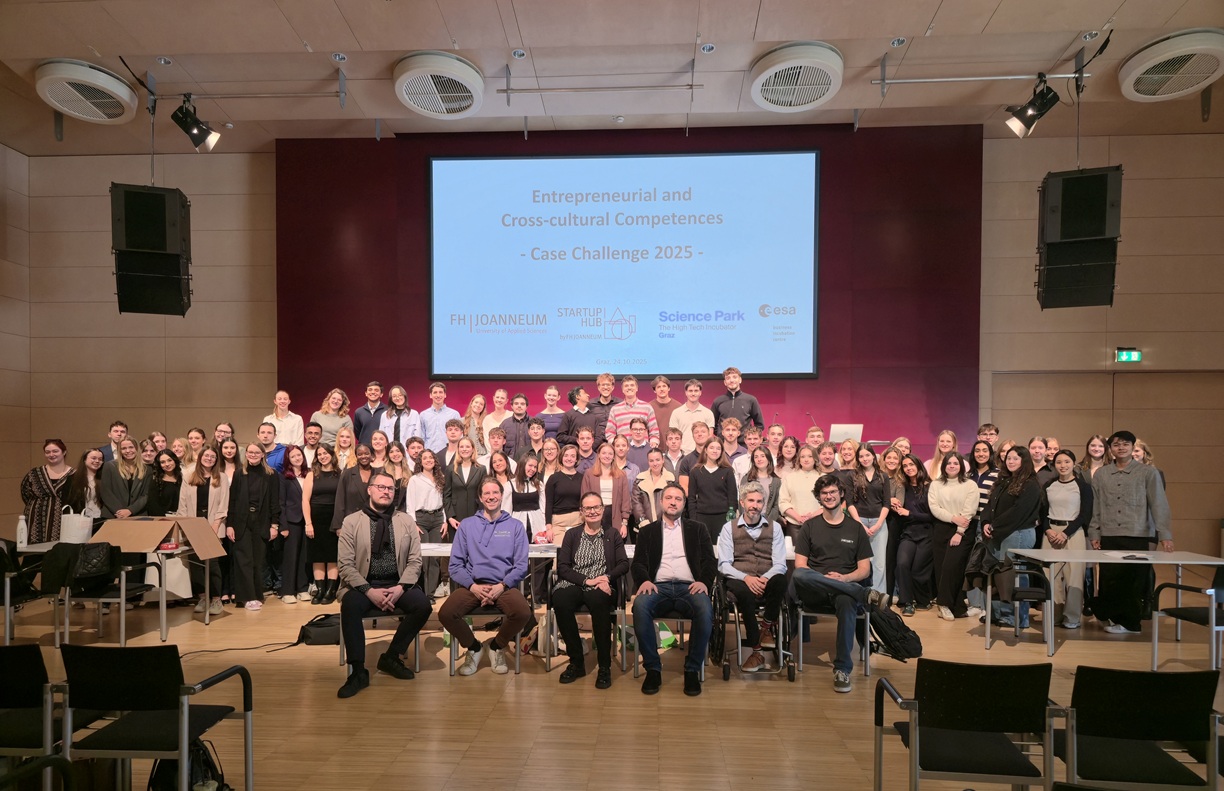 Suuri joukko ihmisiä poseeraa yhdessä auditoriossa näytön edessä, jossa näkyy "Yrittäjyys ja kulttuurienvälinen osaaminen - Case Challenge 2025". Jotkut istuvat, useimmat seisovat ja hymyilevät kameralle.