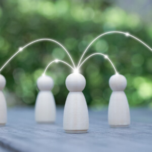 Neljä puista hahmoa on sijoitettu pöydälle ulkona, ja hehkuvat viivat yhdistävät yhden keskushahmon muihin hahmoihin, mikä symboloi viestintää tai verkostoitumista. Tausta on sumea ja vihreä.