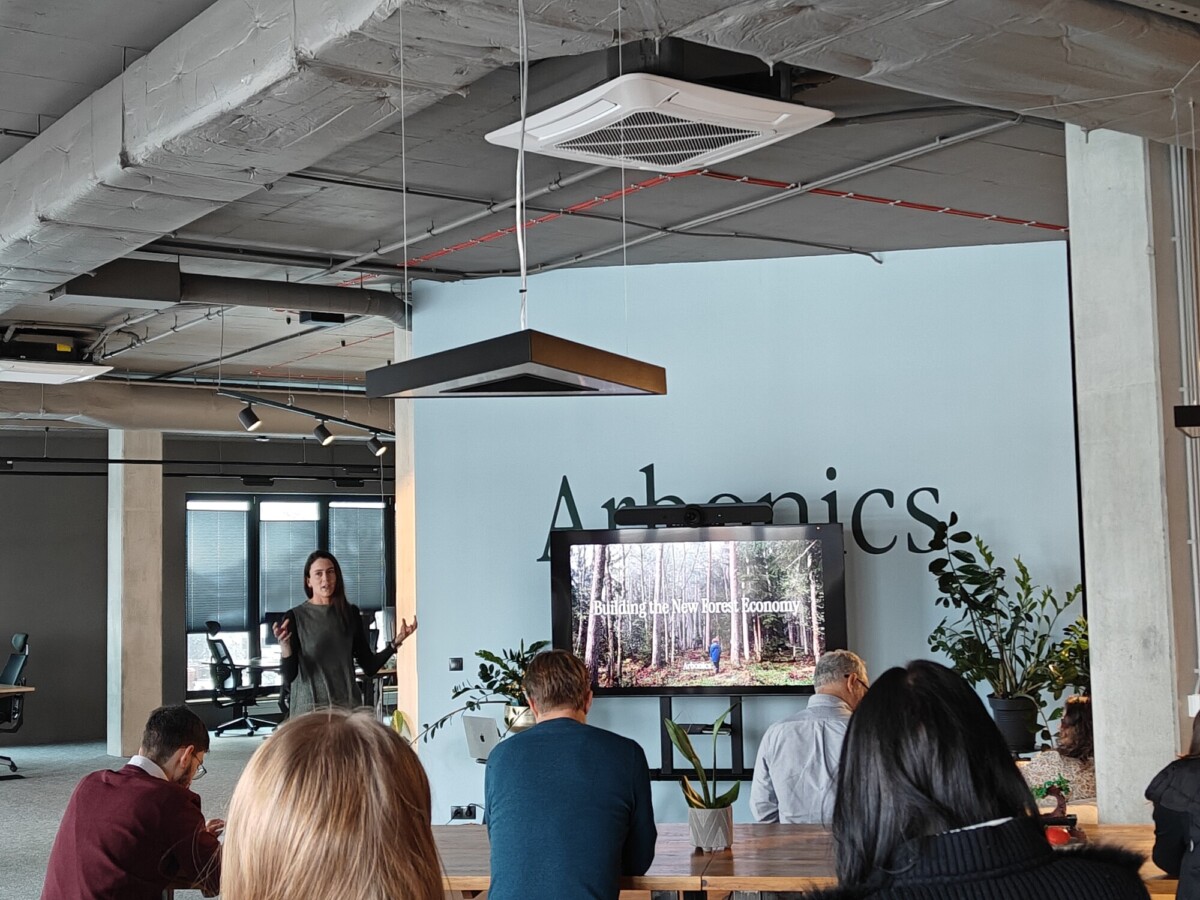 Nainen seisoo ja esittelee näytön edessä, jossa näkyy Building the New Forest Economy, istuvalle ryhmälle modernissa, avoimessa toimistotilassa, jossa on suuret ikkunat, kasveja ja sana Arbionics seinällä.
