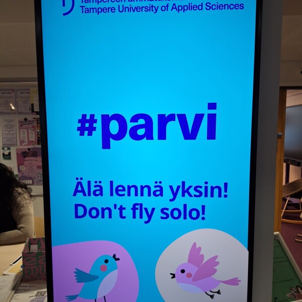 Tampereen ammattikorkeakoulun digitaalisessa kyltissä näkyy #parvi ja viesti Älä lennä yksin! Älä lennä yksin! kuvituksena kaksi lintua ja suuri kukka sinisellä taustalla.