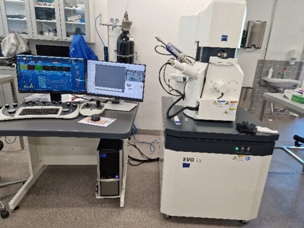 Kuvassa on Pyyhkäisyelektronimikroskooppi Zeissin EVO 15. Laboratoriotyöpiste, jossa on kaksi monitoria, joilla näytetään tieteellisiä tietoja, tietokonetorni, näppäimistö ja suuri valkoinen EVO i3 -elektronimikroskooppi työpöydän vieressä, jota ympäröivät erilaiset laboratoriolaitteet.