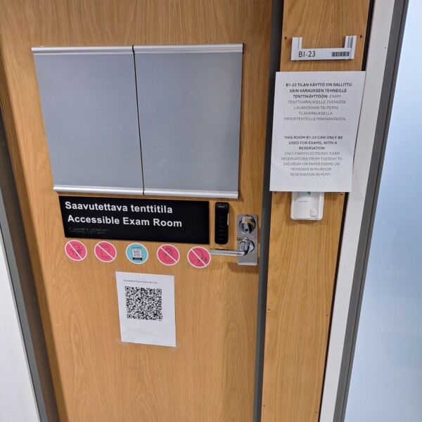 Puuovi, jossa lukee Saavutettava tenttitila / Esteetön tutkimushuone, QR-koodi, elektroninen lukko ja viereisellä seinällä painettu ilmoitus, jossa ilmoitetaan rajoitettu pääsy ja tutkimushuoneen säännöt.