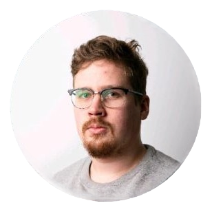 Henkilö, jolla on lyhyet vaaleanruskeat hiukset, parta ja silmälasit, ja jolla on harmaa toppi, katsoo kameraan valkoista taustaa vasten.