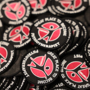 Kasa pyöreitä mustia laastareita, joissa on punavalkoinen abstrakti kuvio ja reunalla valkoisin kirjaimin teksti GREAT PLACE TO BECOME PHYSIOTHERAPIST.