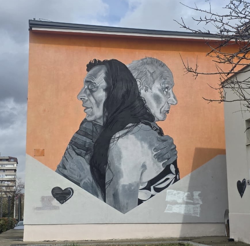 Oranssin rakennuksen seinään kiinnitetty seinämaalauksessa on harmaasävyisinä kuvattu iäkäs mies ja nainen, jotka syleilevät toisiaan. Heidän ilmeensä näyttävät juhlallisilta. Seinään on maalattu kaksi pientä mustaa sydäntä.