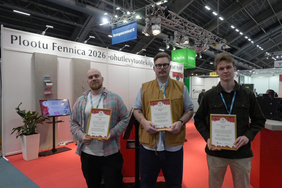 Kolme miestä seisoo sisätiloissa tapahtumassa, ja jokaisella on kädessään todistus. He ovat kojun edessä, jossa on kyltti Plootu Fennica 2026 -ohutlevytuotekilp. Ympäristö näyttää olevan kokouskeskus tai messutapahtuma.