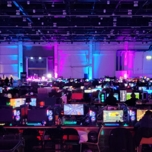 Suuri, hämärästi valaistu sali, joka on täynnä rivejä hehkuvia tietokonemonitoreja ja pelaavia ihmisiä, jotka ovat valaistu eloisilla sinisillä ja violeteilla valoilla ja luovat vilkkaan pelitapahtuman tunnelman.