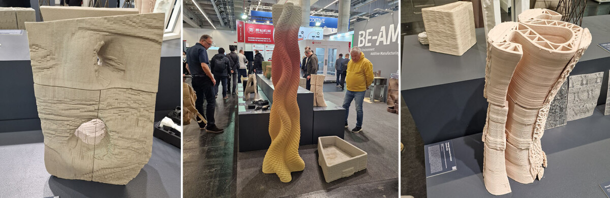 Kolme veistoksellista 3D-tulostettua arkkitehtonista mallia on esillä näyttelyssä, jossa ihmiset kävelevät ympäriinsä ja tarkkailevat teoksia messuosastolla.