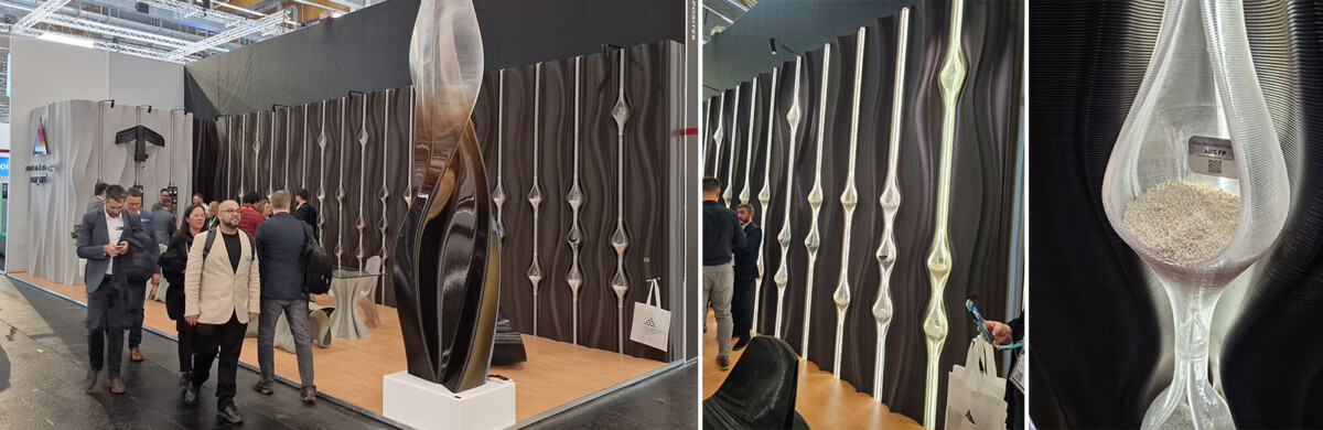 Ryhmä ihmisiä kävelee modernin näyttelynäyttelyn ohi, jossa on korkeita, veistoksellisia mustia paneeleita, joissa on pisaranmuotoisia kirkkaita taskuja, joista yksi sisältää läpinäkyviä granulaatteja.