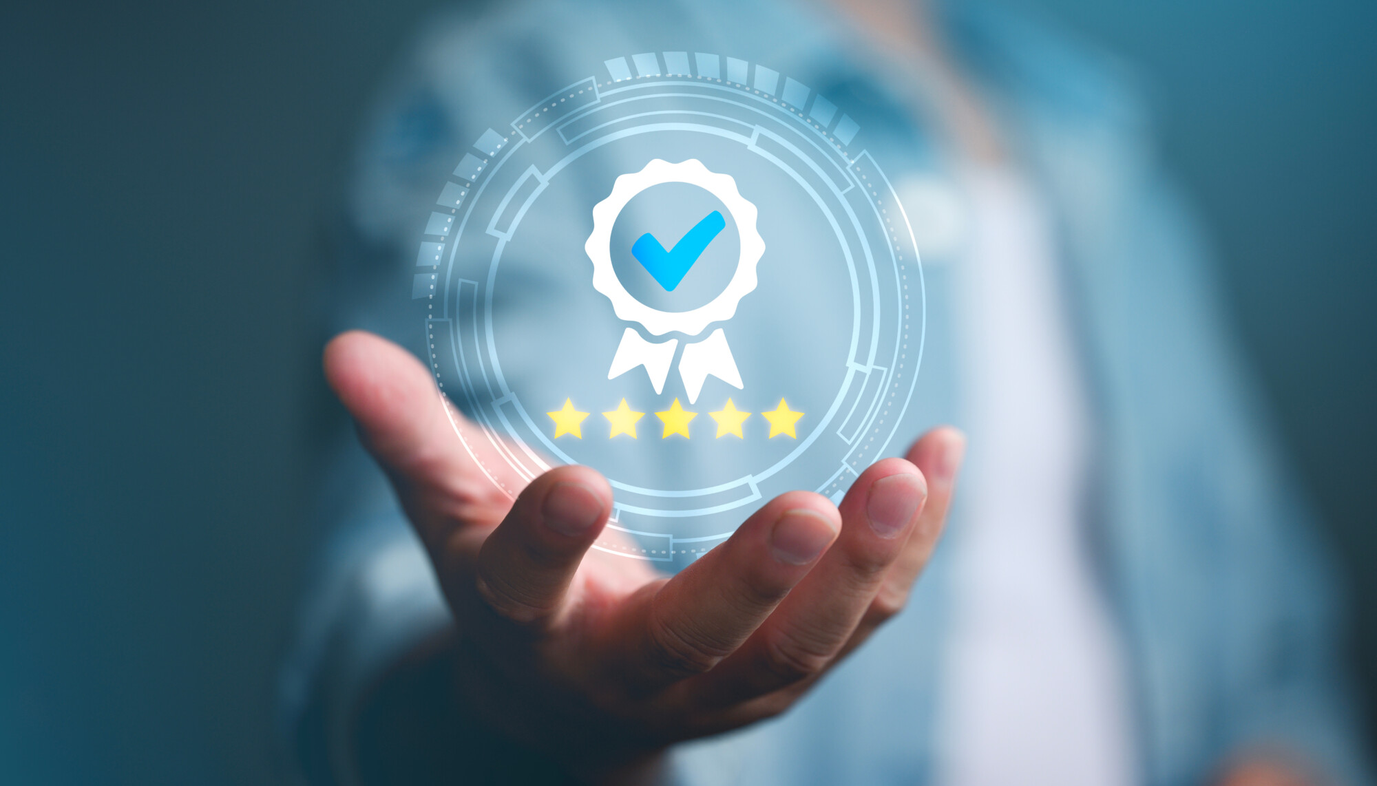 Henkilö ojentaa kätensä, jonka yläpuolella on digitaalinen grafiikka, jossa on ruksi ja viisi kultatähteä, jotka symboloivat laatua, luottamusta tai korkeaa arvosanaa. Tausta on sumea.