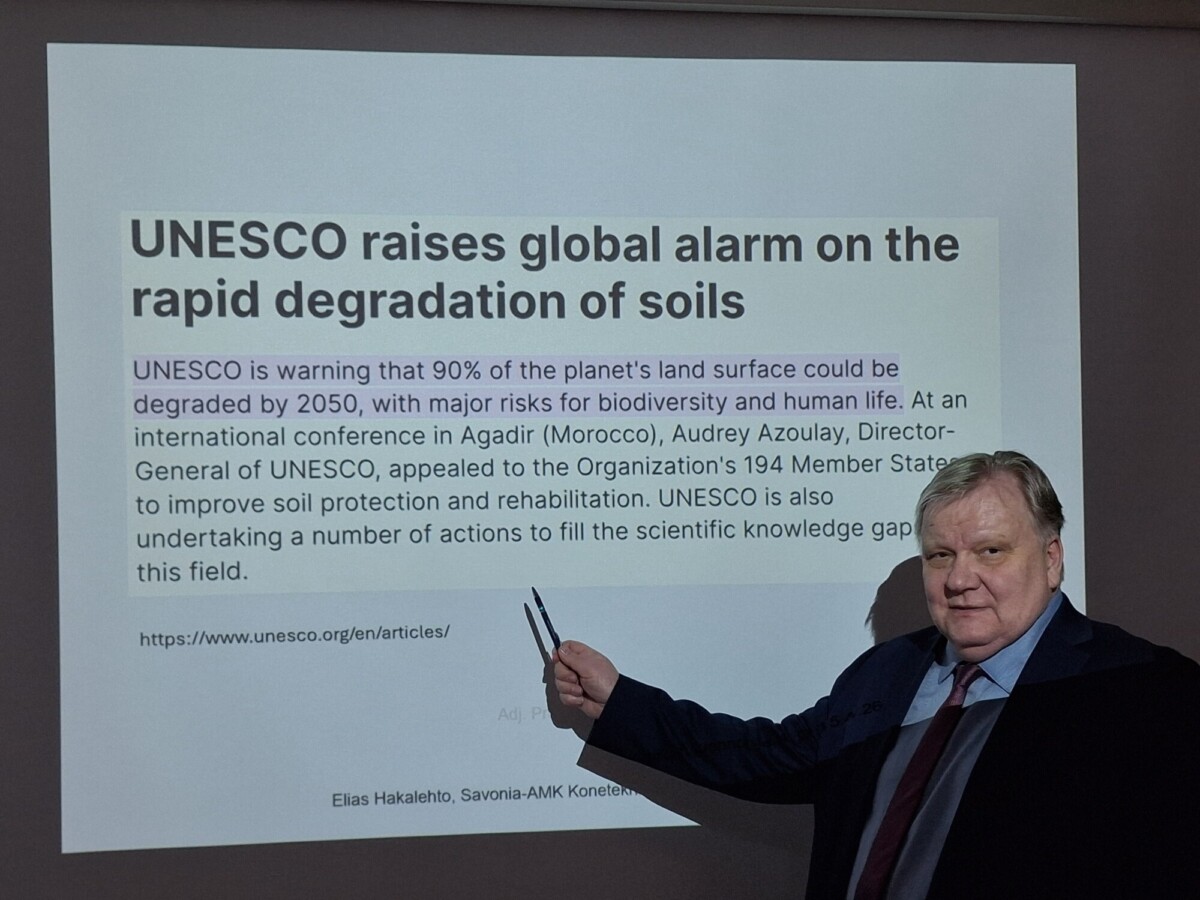 Pukumies osoittaa diaesitystä, jonka otsikkona on Unescon maailmanlaajuinen hälytys maaperän nopeasta heikkenemisestä ja teksti, jossa varoitetaan maaperän heikkenemisestä vuoteen 2050 mennessä.