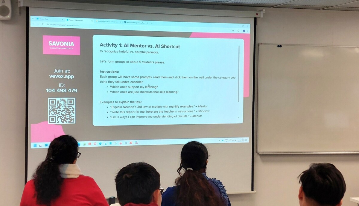 Luokkahuone, jossa kolme ihmistä on vastassaan heijastettu dia, jonka otsikkona on Activity 1: AI Mentor vs. AI Shortcut. Dia sisältää ohjeita, esimerkkejä ja QR-koodin vasemmalla puolella.