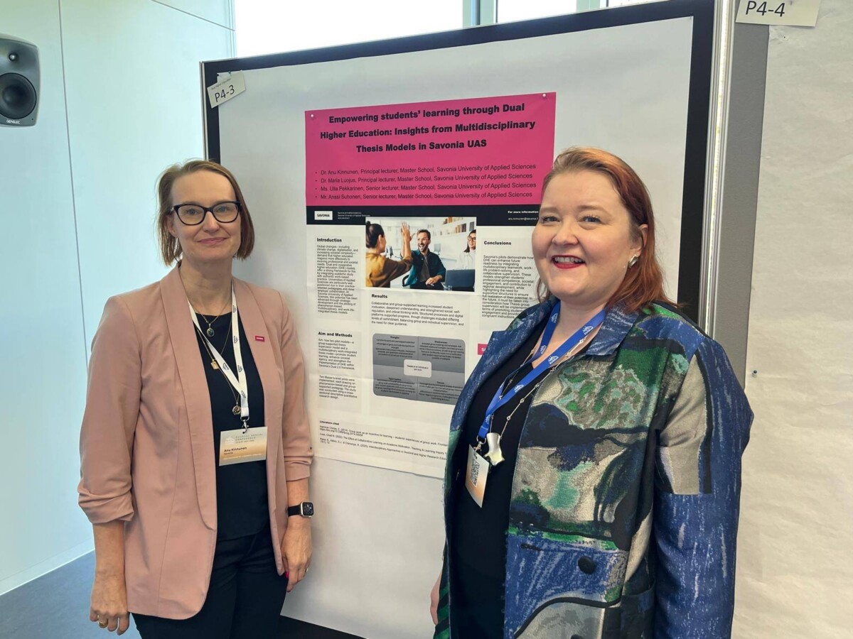 Kaksi naista seisoo hymyillen tutkimusjulisteen edessä, jonka otsikko on Empowering students' learning through Dual Higher Education: Insights from Multidisciplinary Thesis Models in Savonia UAS akateemisessa konferenssissa.