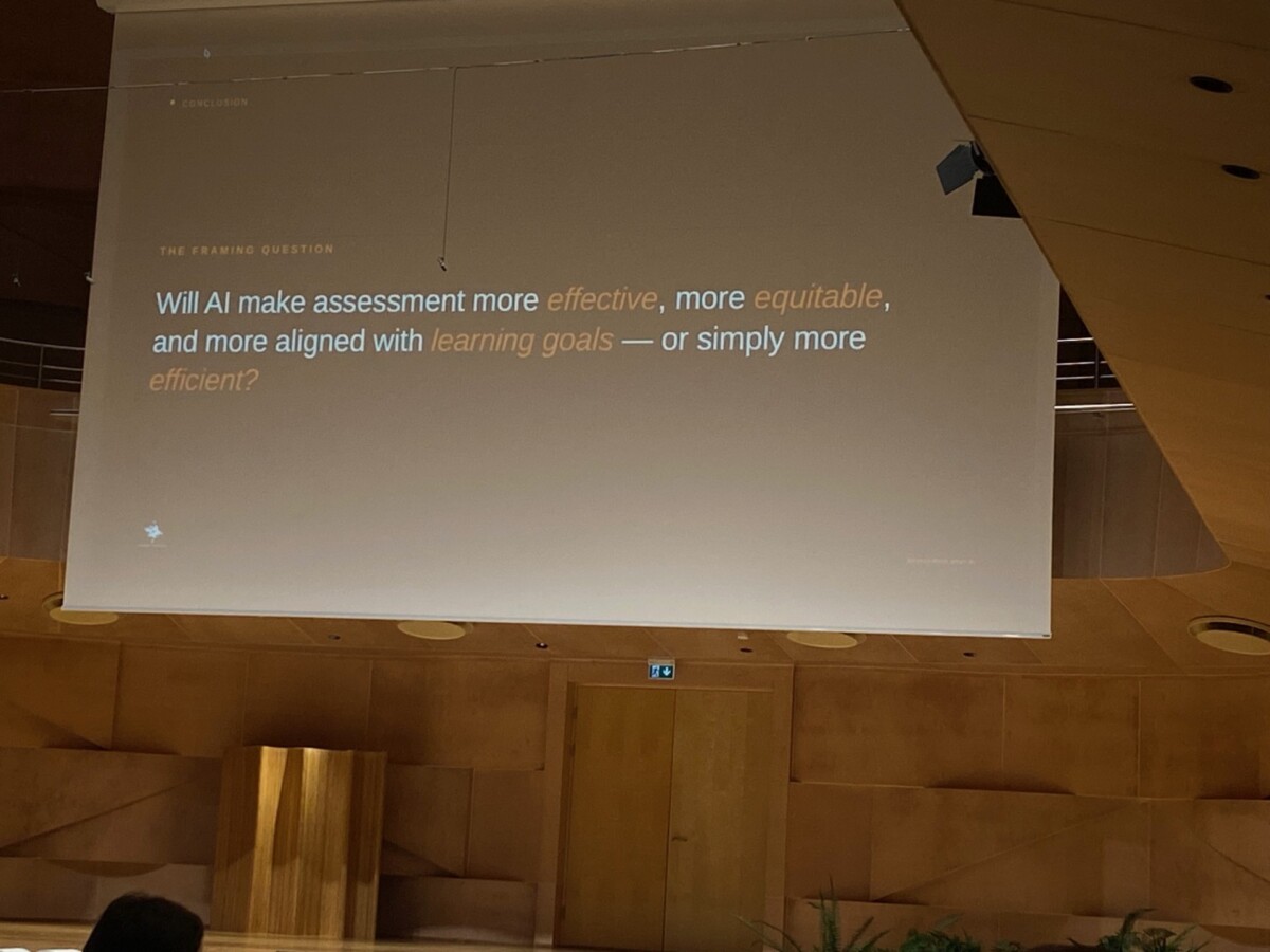 Puisessa auditoriossa on esitysdia, jossa näkyy kysymys: Vai tekeekö tekoäly arvioinnista tehokkaampaa, tasapuolisempaa ja oppimistavoitteita paremmin vastaavaa - vai pelkästään tehokkaampaa?".