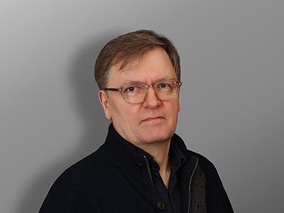 Jukka Onttonen, Keski-ikäinen mies, jolla on lyhyet vaaleanruskeat hiukset ja silmälasit, tumma pusero ja kauluspaita, seisoo harmaan taustan edessä ja katsoo rauhallisesti kameraan.