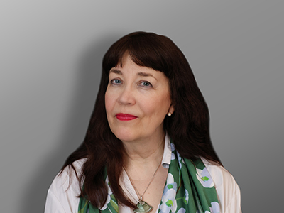 Katariina Liimatainen, Nainen, jolla on pitkät tummanruskeat hiukset ja vaalea iho, yllään valkoinen toppi, vihreä kukkahuivi ja kaulakoru, poseeraa harmaata taustaa vasten.