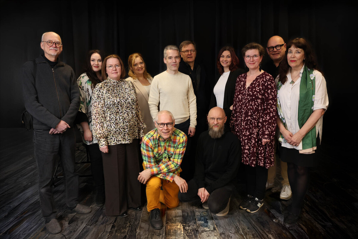 Kuvassa Savonian henkilökuntaa. Musiikin opetus. Kolmetoista aikuista poseeraa yhdessä sisätiloissa tummalla lattialla, jossa on musta tausta. Useimmat seisovat, kun taas kaksi miestä polvistuu edessä. Kaikki ovat pukeutuneet rennosti tai tyylikkäästi ja katsovat kameraan päin.