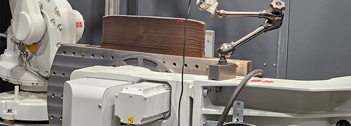 Lähikuva teollisuusrobotista, jossa on metalliset käsivarret ja kerroksellinen materiaali, jota käytetään todennäköisesti valmistukseen tai testaukseen laboratorio- tai tehdasympäristössä.