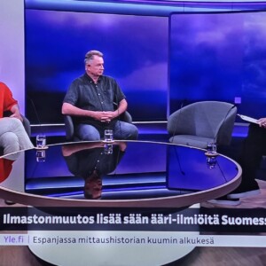 Kolme henkilöä istuu televisiostudion lavastuksessa keskustelemassa ilmastonmuutoksesta. Kaksi vierasta istuu pyöreän lasipöydän ääressä kaljupäistä juontajaa vastapäätä. Ruudulla näkyy suomenkielistä tekstiä ja uutisnauha, jossa on violetteja ja keltaisia graafisia elementtejä.