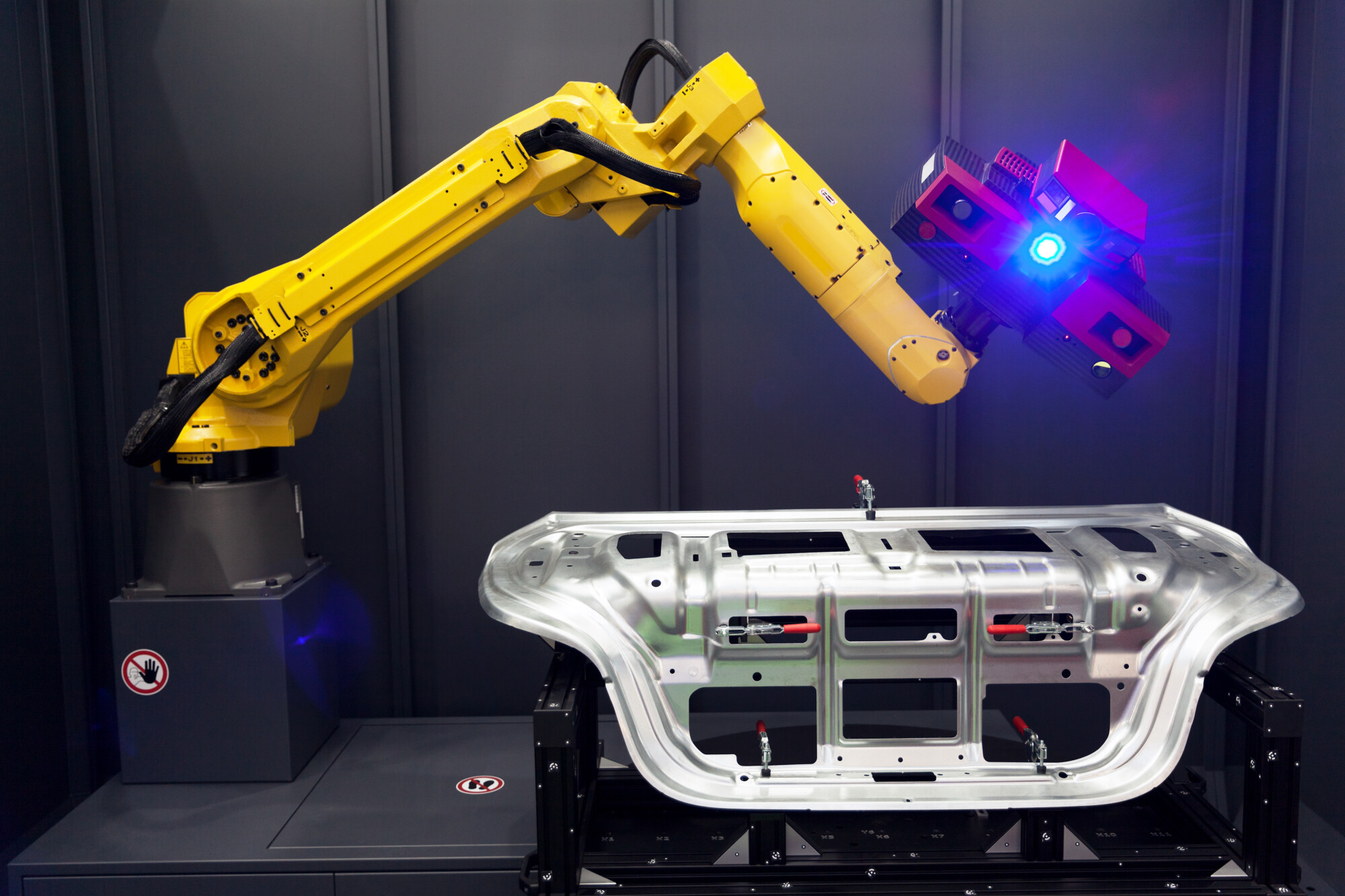 Keltainen robottivarsi, jossa on sininen valo, skannaa metallista auton osaa mustalla alustalla teollisuusympäristössä.