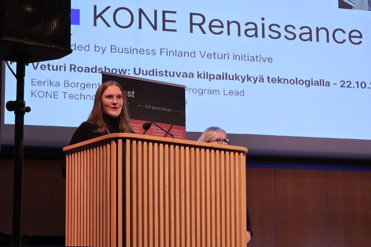 Nainen puhuu puhujakorokkeella KONE Renaissance ja Veturi Roadshow -nimisen esitysdian edessä.