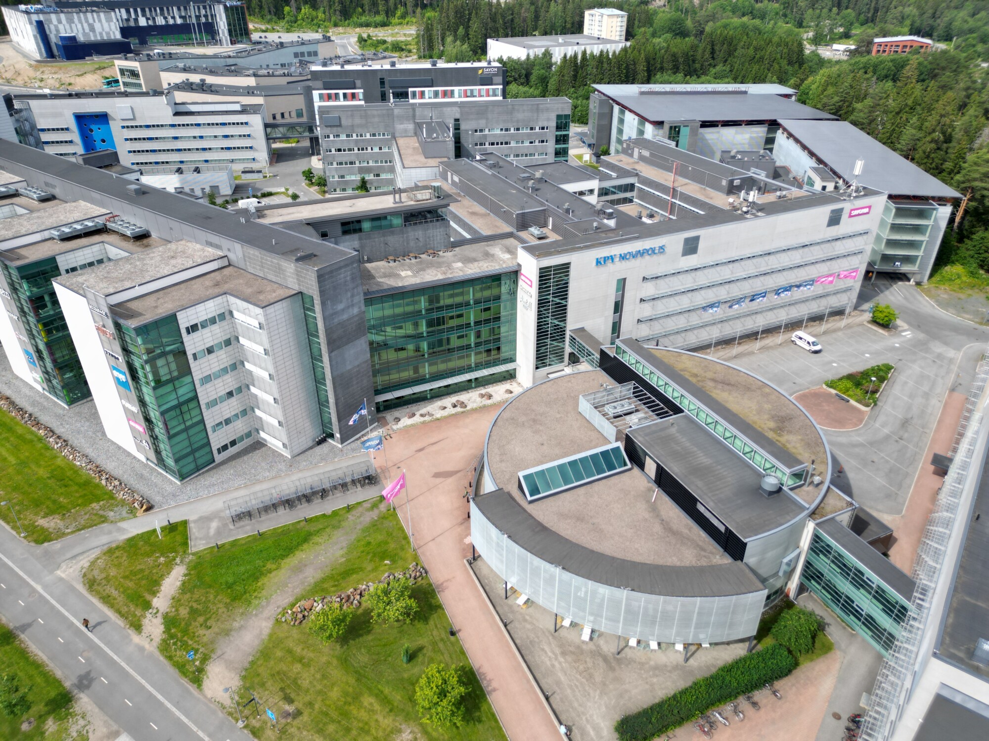 Ilmakuva vehreän ympäristön keskellä sijaitsevasta modernista sairaalakompleksista, jossa on useita toisiinsa yhteydessä olevia rakennuksia, lasijulkisivut, pysäköintialueet ja lähellä kulkevat tiet.