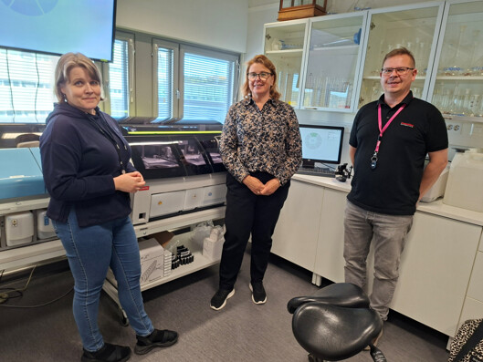 Kolme henkilöä seisoo laboratoriossa automatisoidun testauslaitteen vieressä.